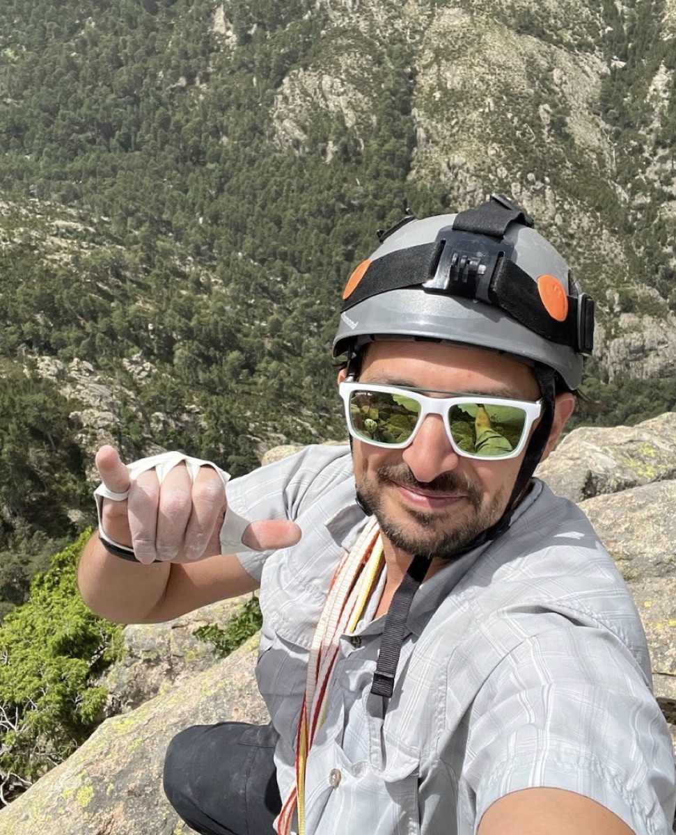 Avi in a climbing helmet on a rock ledge high above a forested valley